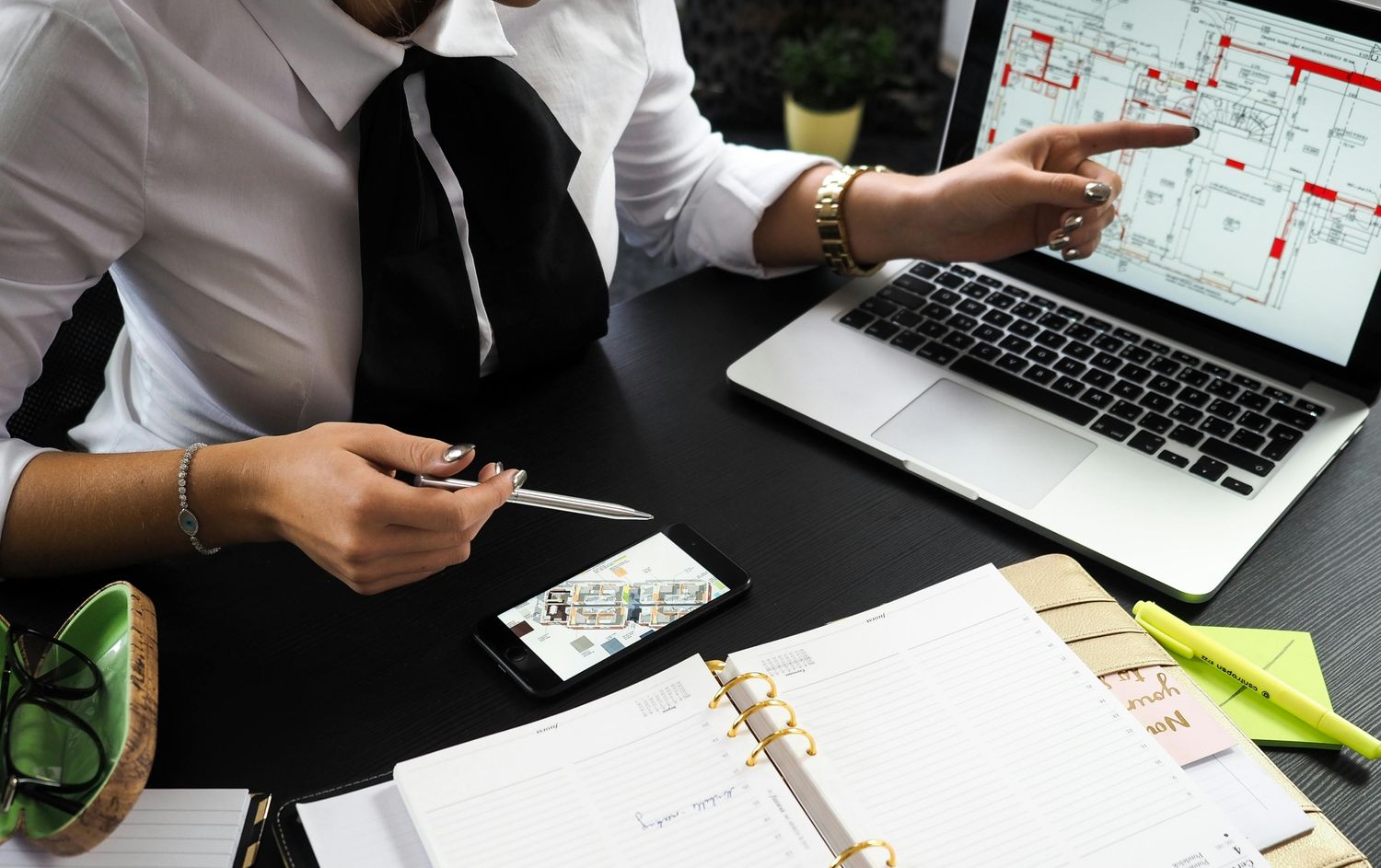 A business professional working on real estate project plans using multiple devices in an office setting.